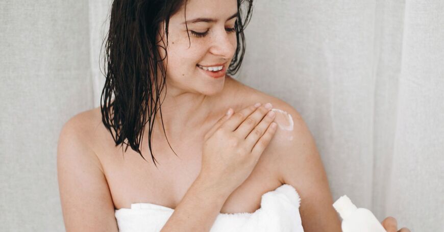 nainen voitelee kosteusvoiteella ihoa suihkun jälkeen